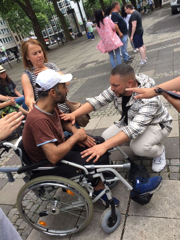 Friends kneeling to pray with a man in a wheelchair on a city street