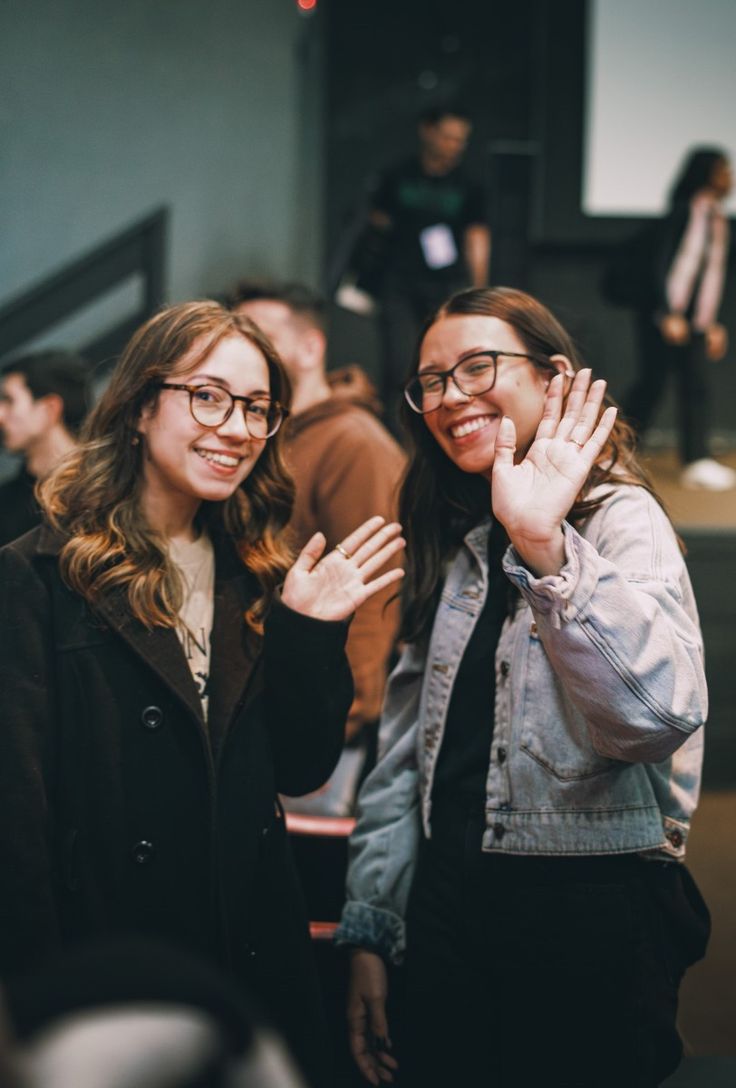 Two friends smiling and waving at a gathering